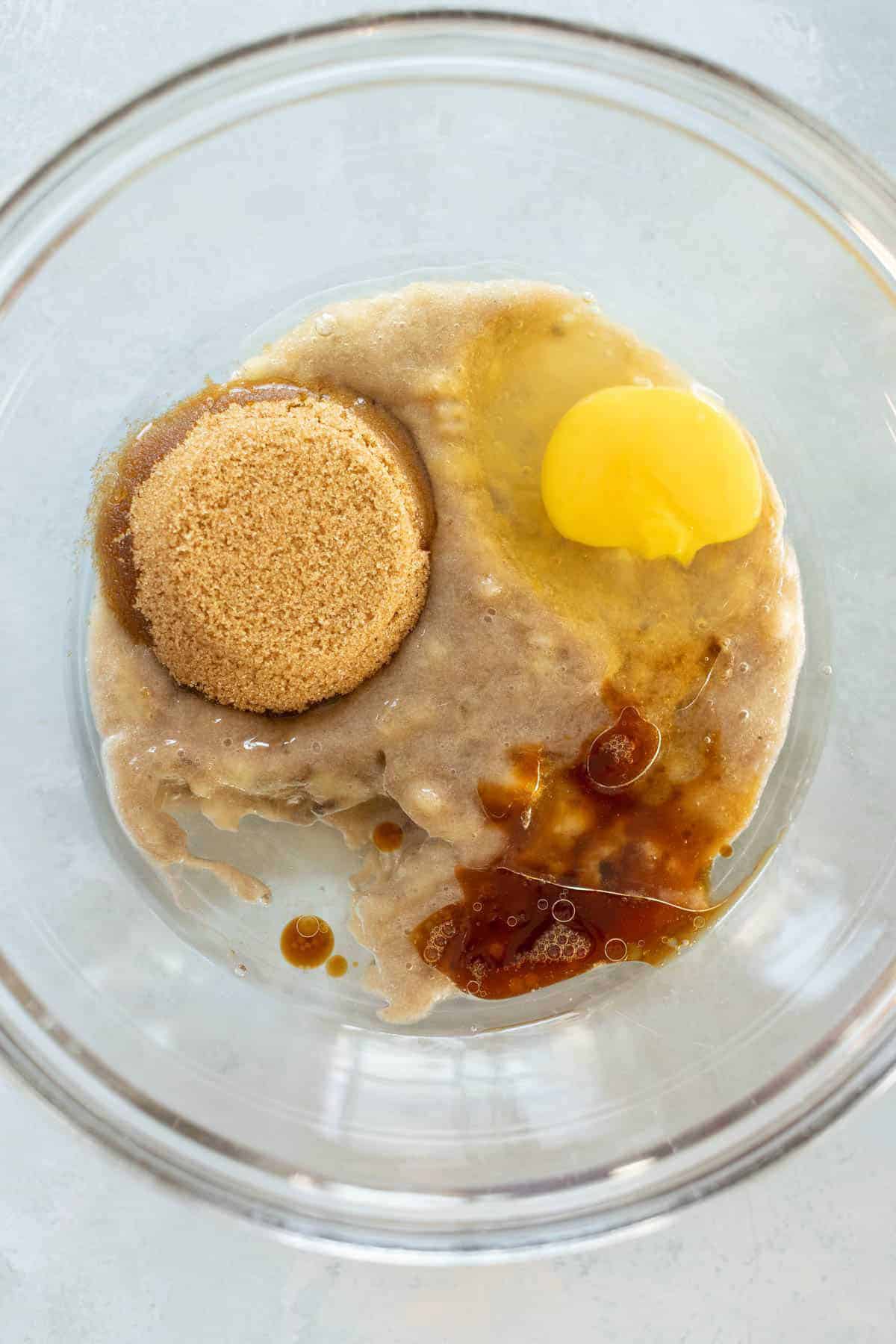 A mixing bowl containing brown sugar, an egg, vanilla extract.