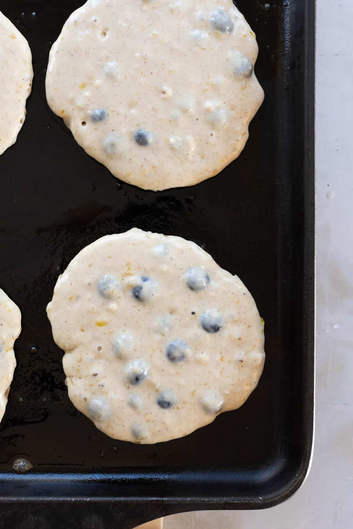 Uncooked blueberry pancakes on a black griddle.