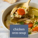 A steaming bowl of chicken orzo soup brimming with carrots and herbs, a spoon lifting a flavorful portion above the bowl. In the background, a piece of crusty bread waits to complete this comforting meal.
