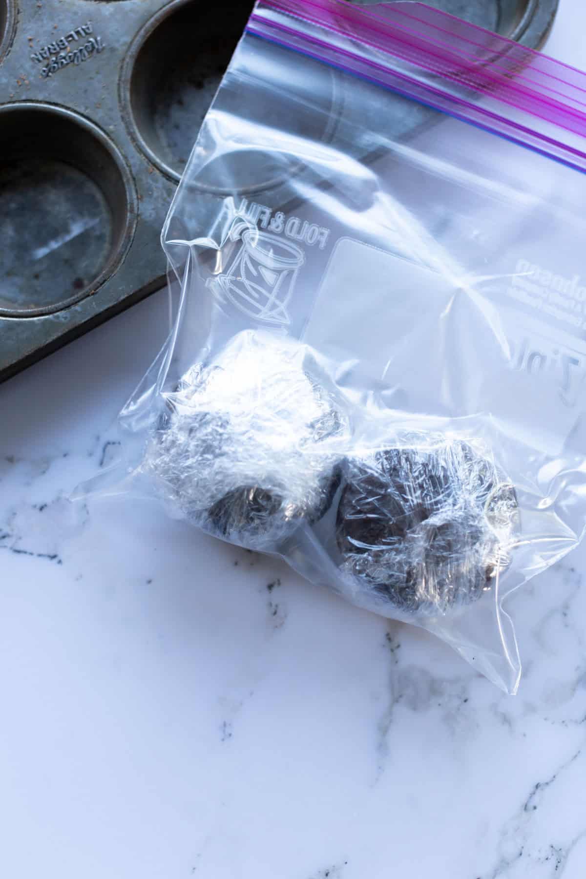 Two foil-wrapped items in a resealable plastic bag next to a muffin tin on a marble surface.