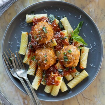 A grey plate of rigatoni topped with ricotta meatballs, parmesan and herbs.