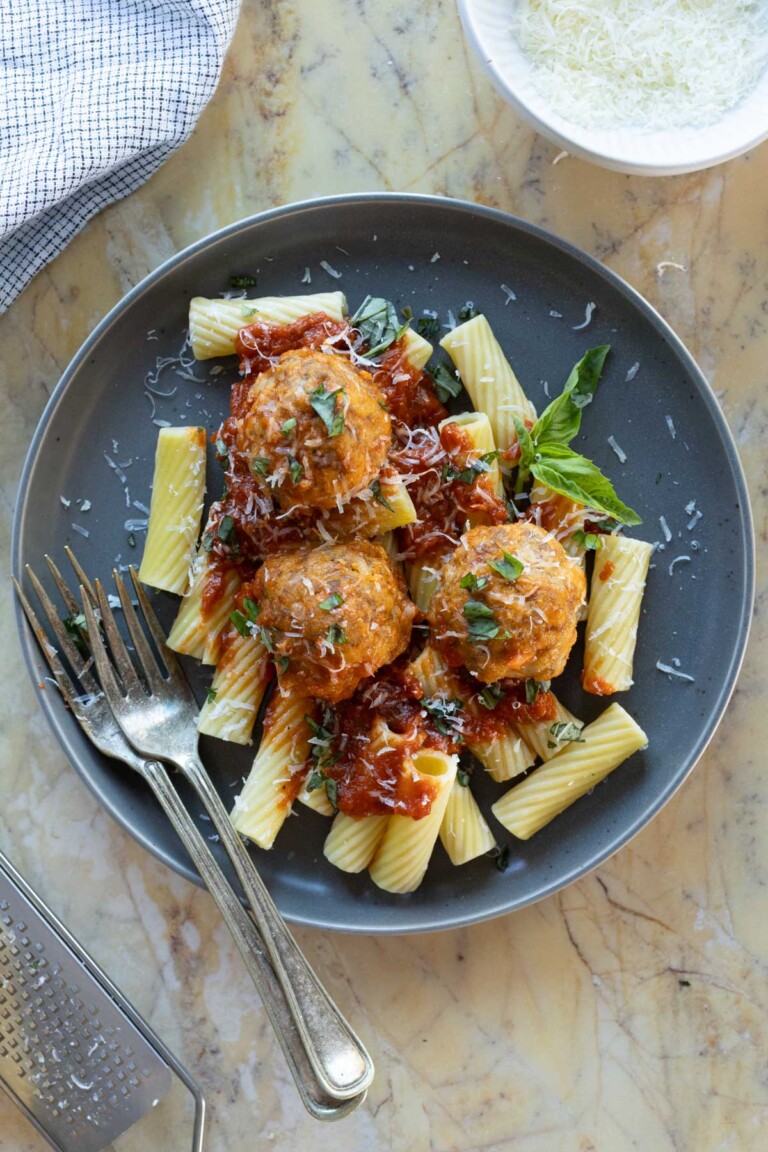 A grey plate of rigatoni topped with ricotta meatballs, parmesan and herbs.