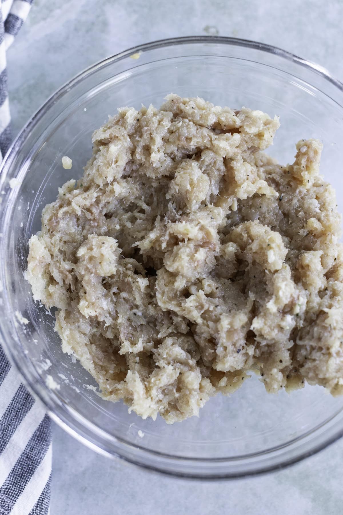 Glass bowl containing mashed bananas on a marble surface, next to a striped cloth.