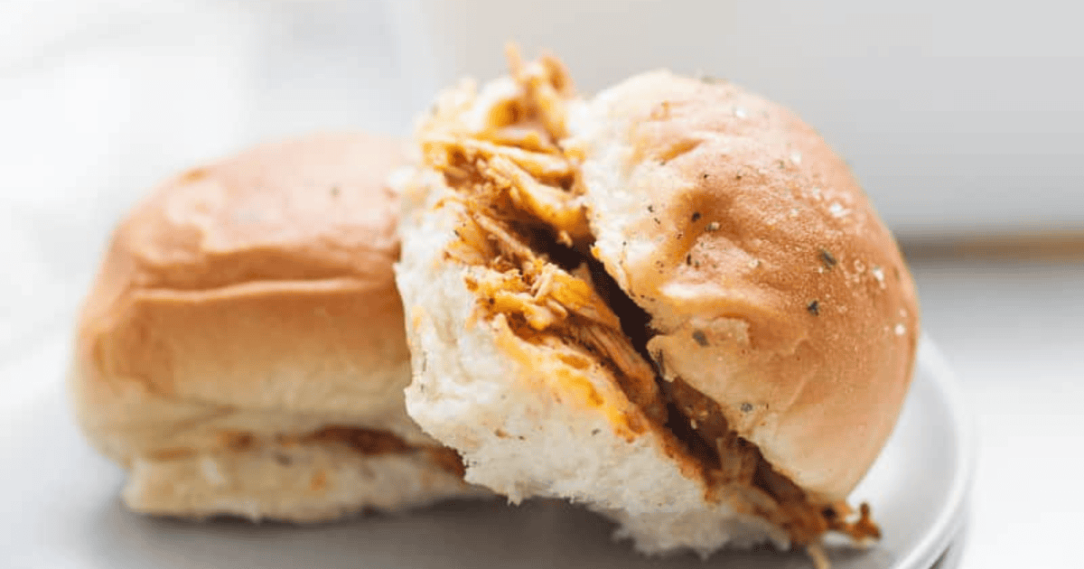 Two chicken sliders with shredded meat on soft buns, served on a white plate.