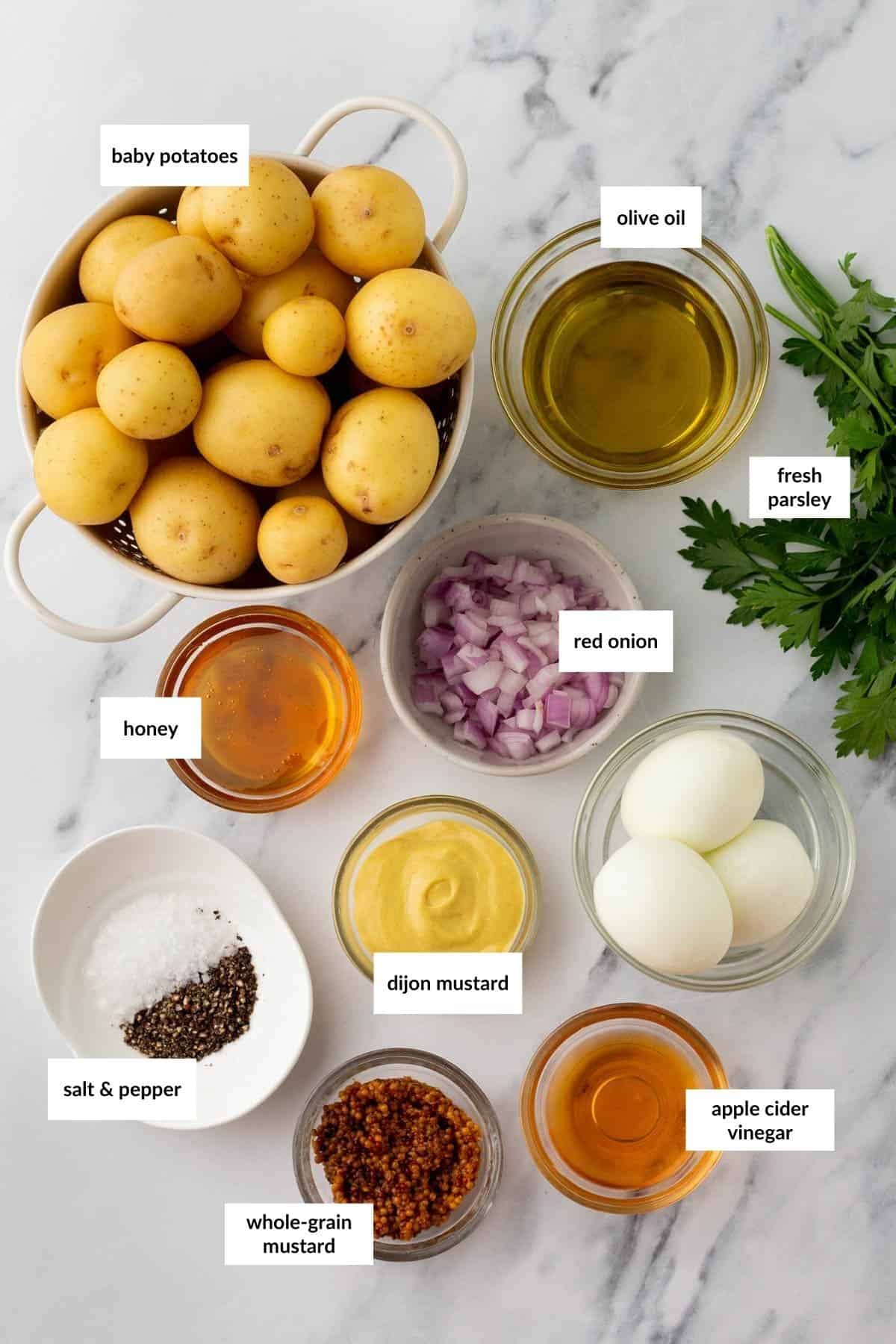 Ingredients for a potato salad: baby potatoes, olive oil, red onion, fresh parsley, honey, dijon mustard, whole-grain mustard, apple cider vinegar, salt, pepper, and hard-boiled eggs.