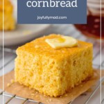 A slice of cornbread topped with butter rests on a cooling rack, while "homemade cornbread bliss" floats above. Nearby, the vibrant promise of a cherry smoothie adds a splash of color to this cozy scene.