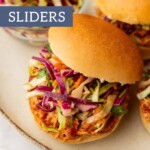 Close-up of BBQ chicken sliders with slaw on a plate. The text reads "BBQ CHICKEN SLIDERS," while "joyfullymad.com" is elegantly displayed at the bottom, inviting you to savor the flavorful experience.