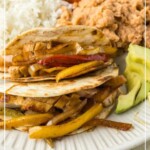 Plate of fajitas with grilled vegetables, rice, beans, avocado, and salsa. Text overlay reads "joyfullymad.com for the best Cinco de Mayo recipes," featuring BBQ chicken sliders as a must-try delight.