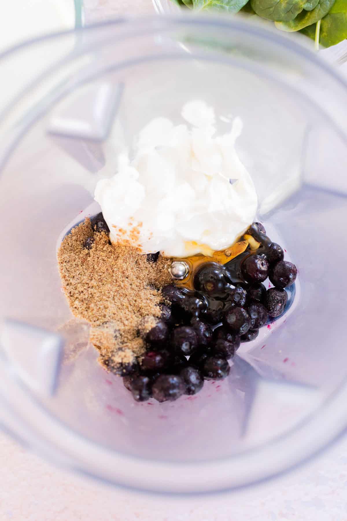 Blender jar with blueberries, flaxseed, yogurt, and honey.