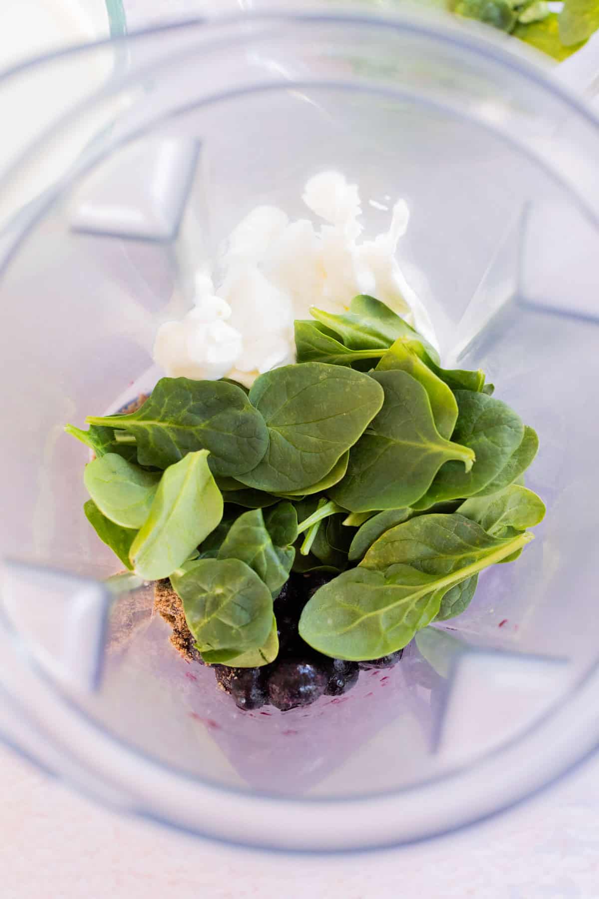 Blender with spinach leaves, and Greek yogurt inside, viewed from above.