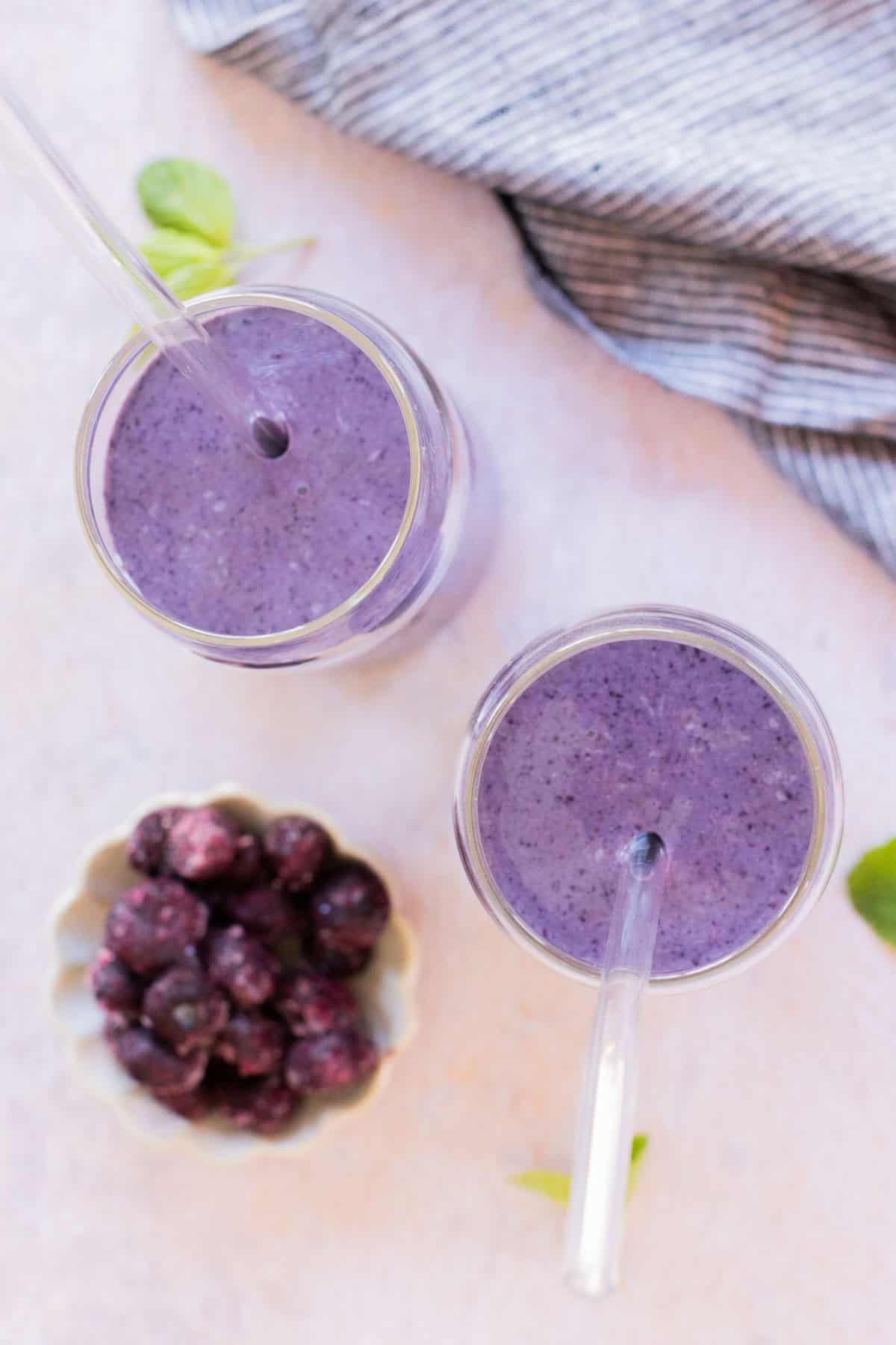 Two glasses of purple Greek yogurt smoothie, shown from above. A jar of frozen berries sits next to the smoothies.