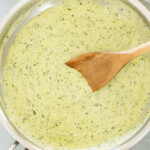 A saucepan filled with creamy pesto sauce, being stirred with a wooden spoon.