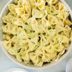 A bowl of creamy pesto pasta mixed set on a light gray surface.