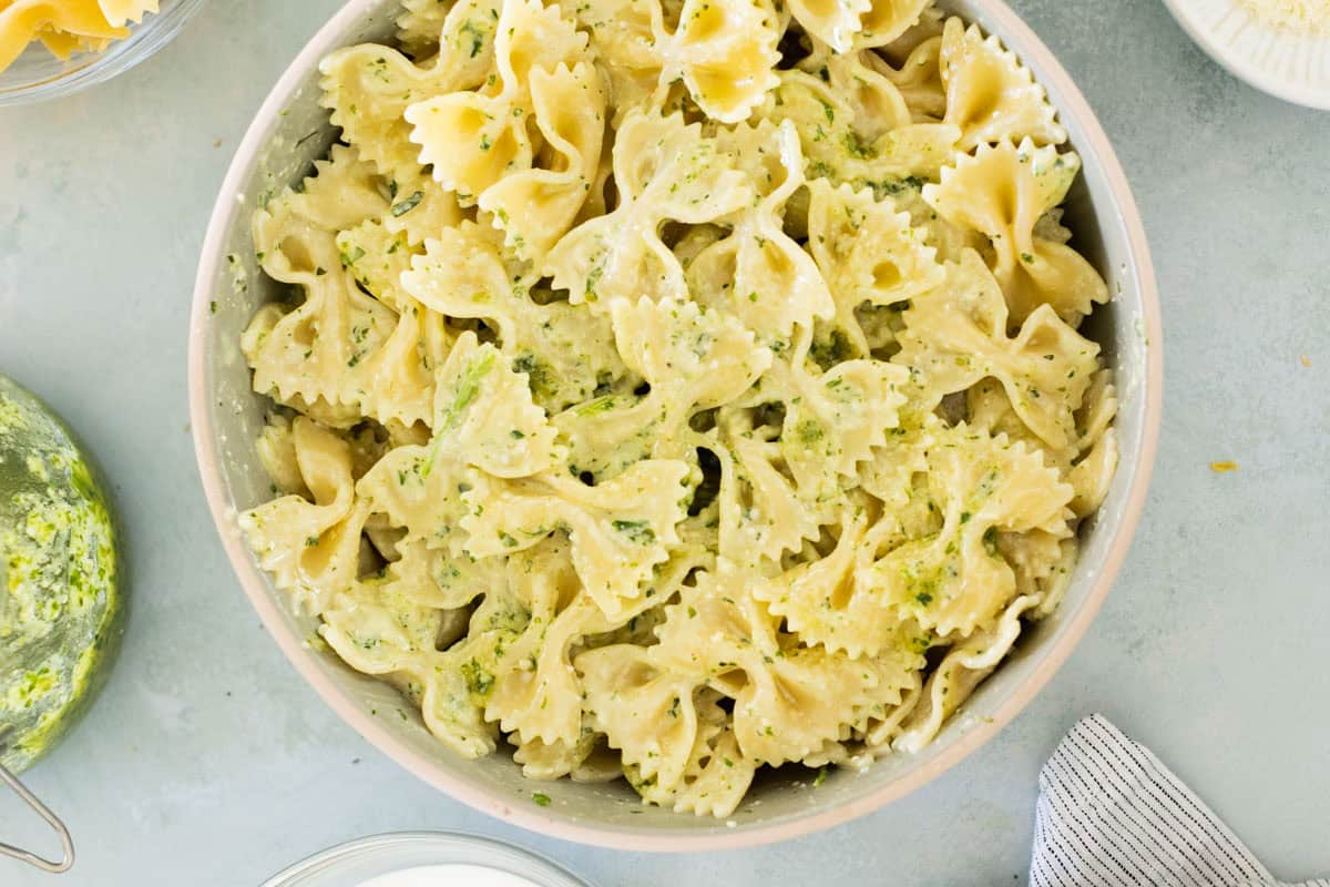 A bowl of creamy pesto pasta mixed set on a light gray surface.