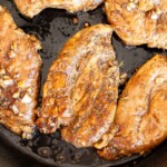 Chicken breasts marinated with garlic and herbs are cooking in a black skillet.