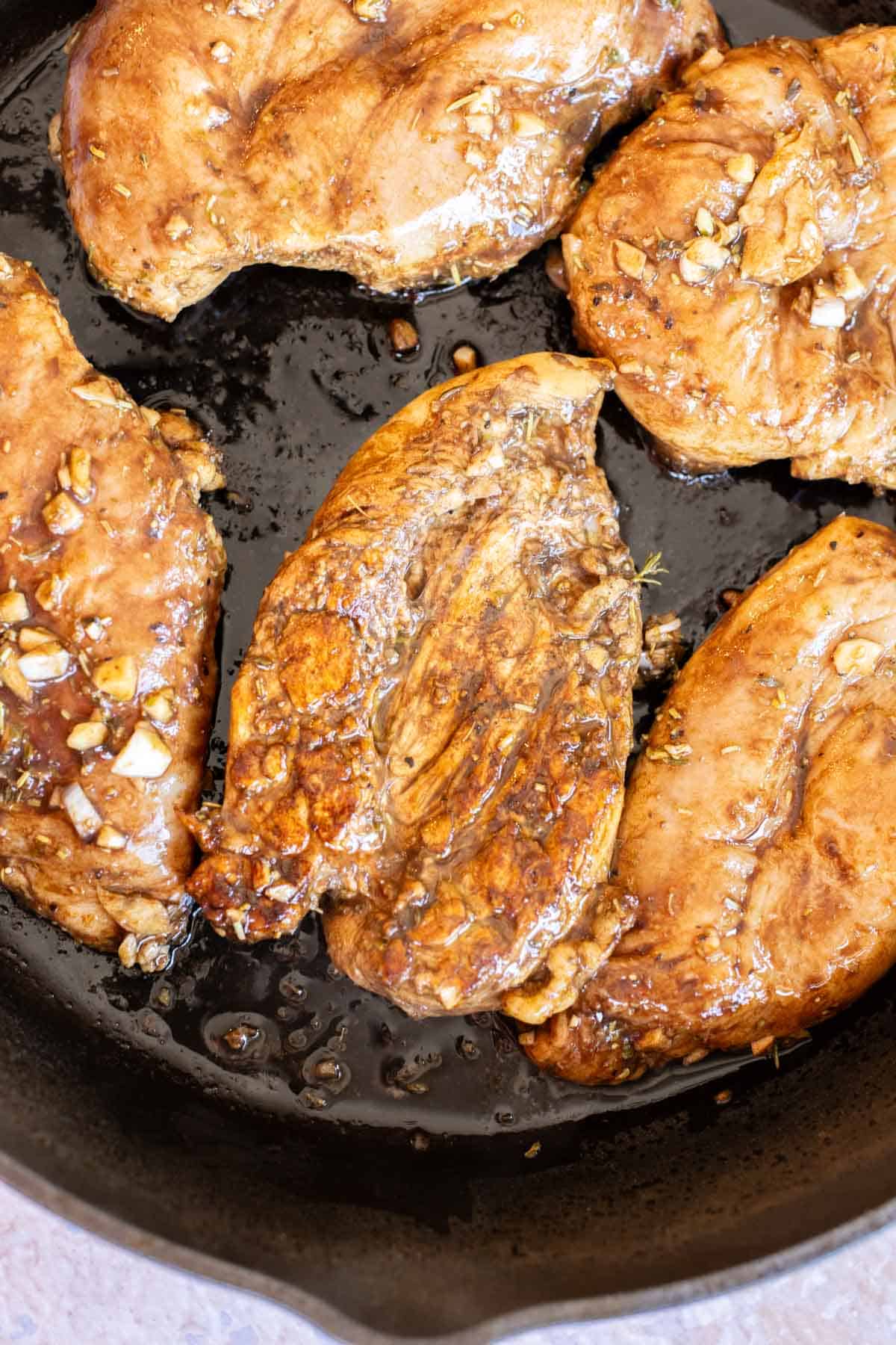 Chicken breasts marinated with garlic and herbs are cooking in a black skillet.