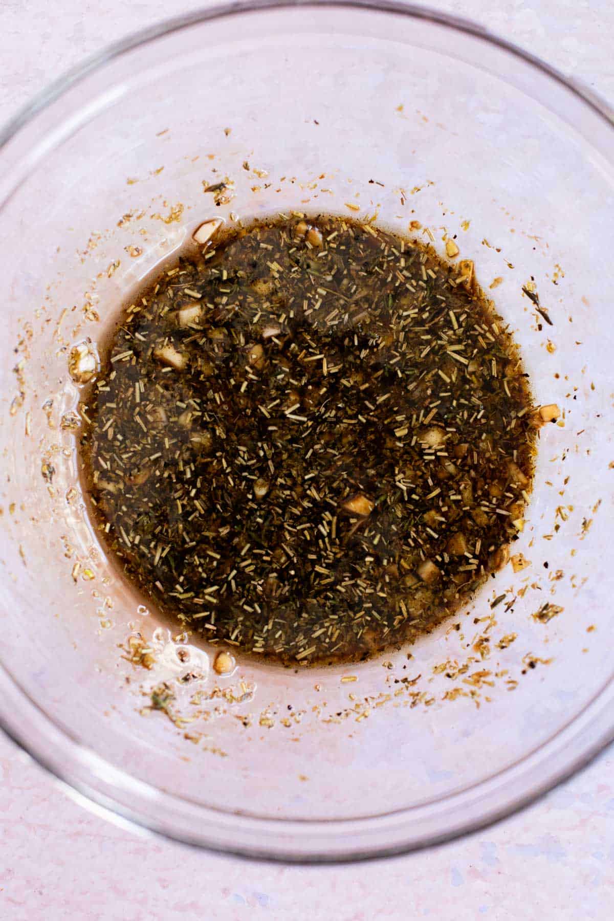 A glass bowl containing a mixture of herbs, spices, and balsamic vinegar, possibly a marinade or dressing.