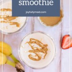 Two glasses of oatmeal smoothie topped with a peanut butter drizzle sit invitingly. Nearby, bananas, a strawberry, and a dish of peanut butter are artfully arranged on a rustic wooden surface, evoking the rich aromas reminiscent of balsamic chicken's culinary creativity.