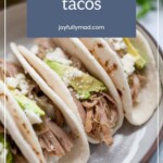 Three soft tacos overflowing with savory pulled pork, creamy avocado, and melted cheese rest on a plate. A text overlay announces "Pulled Pork Tacos" with a website address below, inviting you to experience this tantalizing delight.