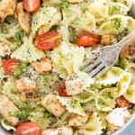 Bowl of bowtie pasta mixed with grilled chicken pieces, cherry tomatoes, and pesto, with a fork in the pasta.
