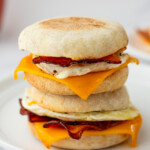 Two breakfast sandwiches with eggs, bacon, and melted cheddar cheese stacked on a white plate.