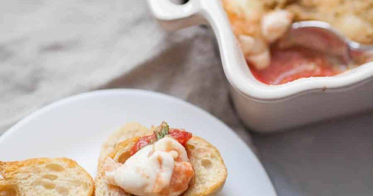 A small toast topped with shrimp and sauce on a plate, next to a casserole dish with a spoon.