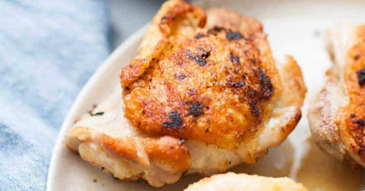 Close-up of cooked chicken thighs with crispy, golden-brown skin on a plate.