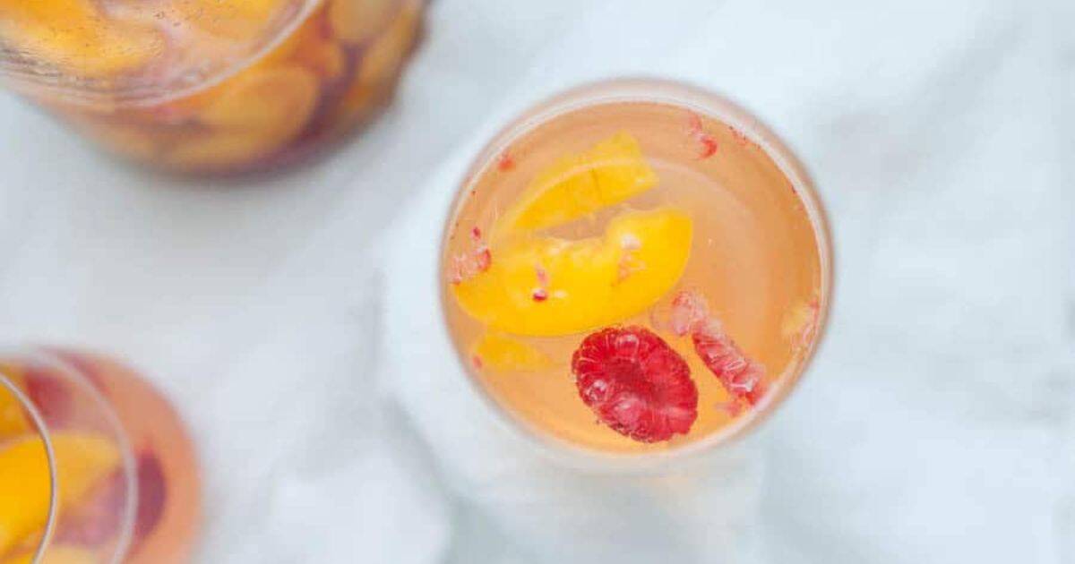 A glass of clear liquid with slices of peach and a raspberry floating inside, viewed from above.