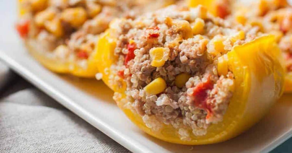 Stuffed yellow bell peppers filled with quinoa, corn, and diced tomatoes on a white plate.