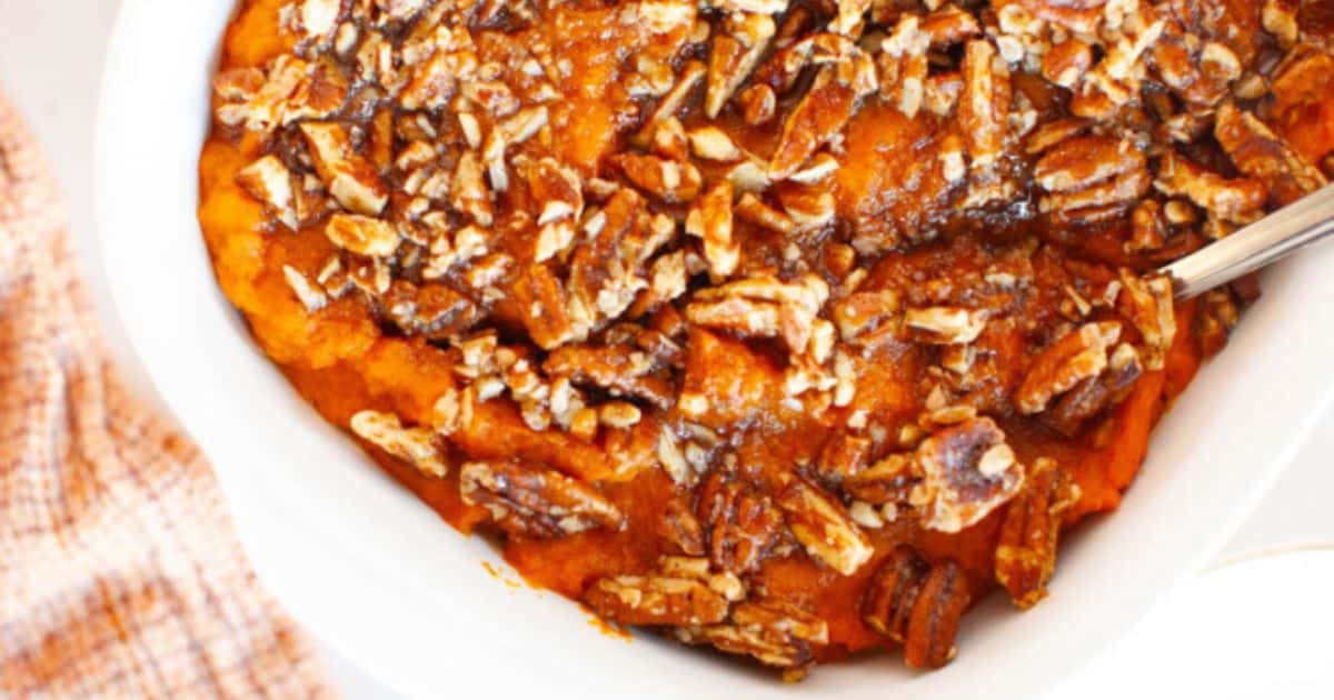 A close-up of a baked sweet potato casserole topped with chopped pecans and a brown sugar glaze in a white dish.