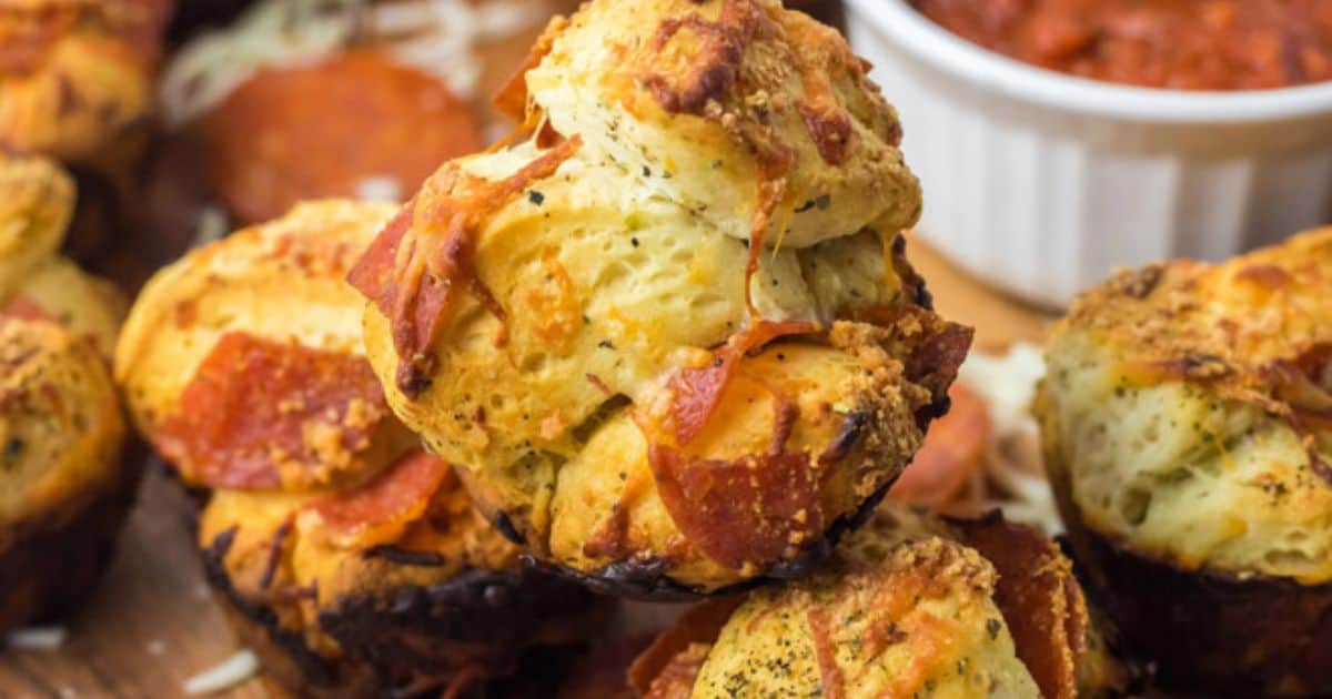 Crispy baked pizza muffins, shown close up next to a cup with marinara dipping sauce.