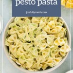 A bowl of creamy pesto pasta made with farfalle, surrounded by bowls of parmesan cheese and extra pesto.
