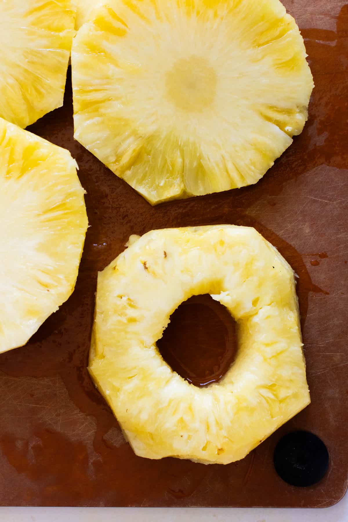 Sliced rings of fresh pineapple with the core removed, placed on a brown cutting board.