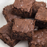 A plate of six chocolate, homemade brownies topped with a sprinkle of coarse salt.