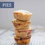 A stack of four mini pies sits on a wire cooling rack, showcasing delicious golden crusts. Text overlay reads "mini pies" and "joyfullymad.com" at the bottom.