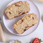 Two slices of strawberry bread are on a white plate. Next to the plate are fresh strawberries and a small dish with lemon wedges.