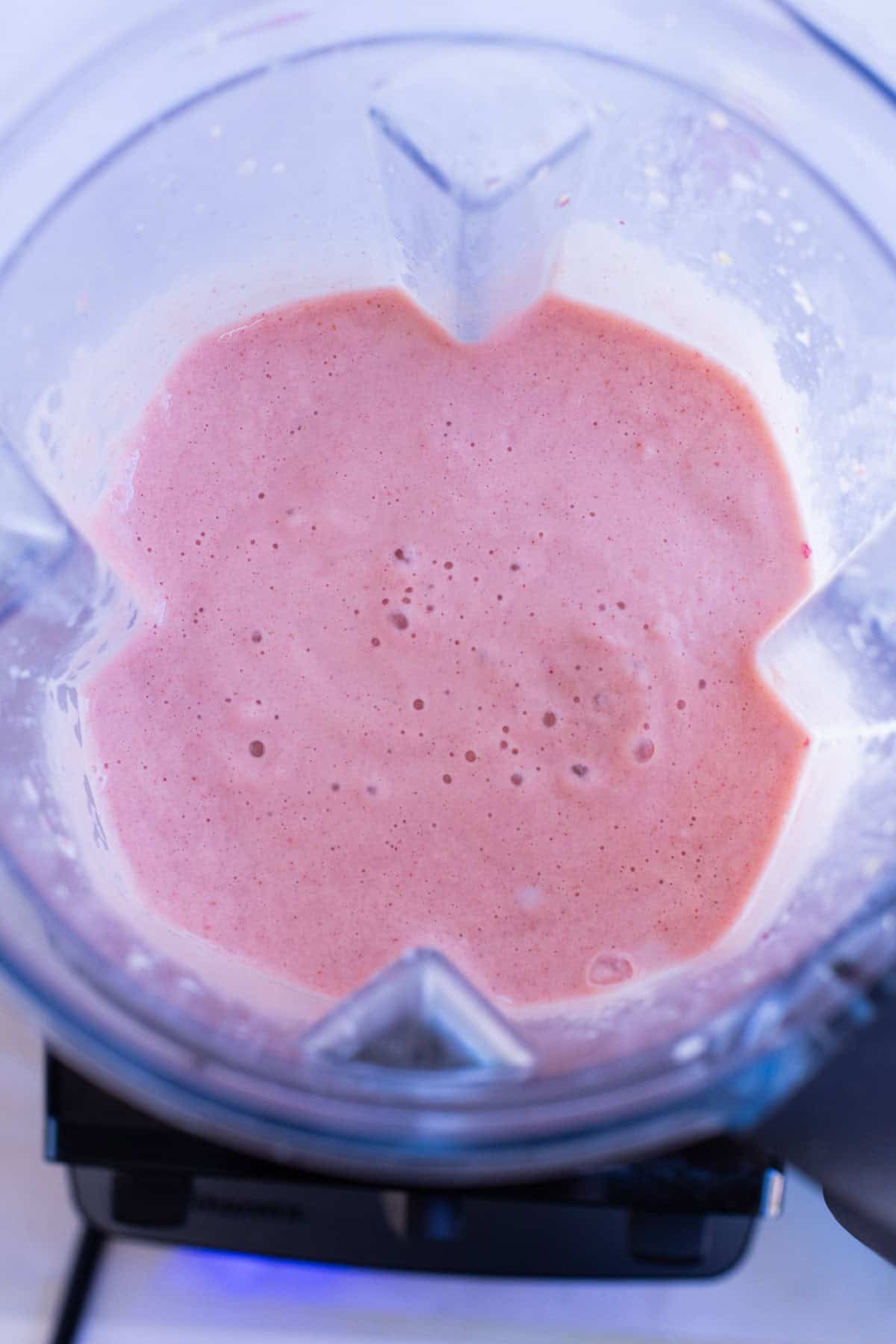 A top-down view of a blender filled with a creamy pink smoothie mixture.