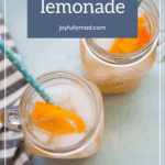 Two mason jars filled with ice, orange lemonade, and orange slices sit beside a striped cloth—perfectly refreshing to pair with turkey lettuce wraps. Each drink is topped with a blue polka dot straw for a playful touch.