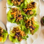 A white platter with turkey lettuce wraps filled with ground meat, shredded carrots, and purple cabbage, garnished with chopped green onions.