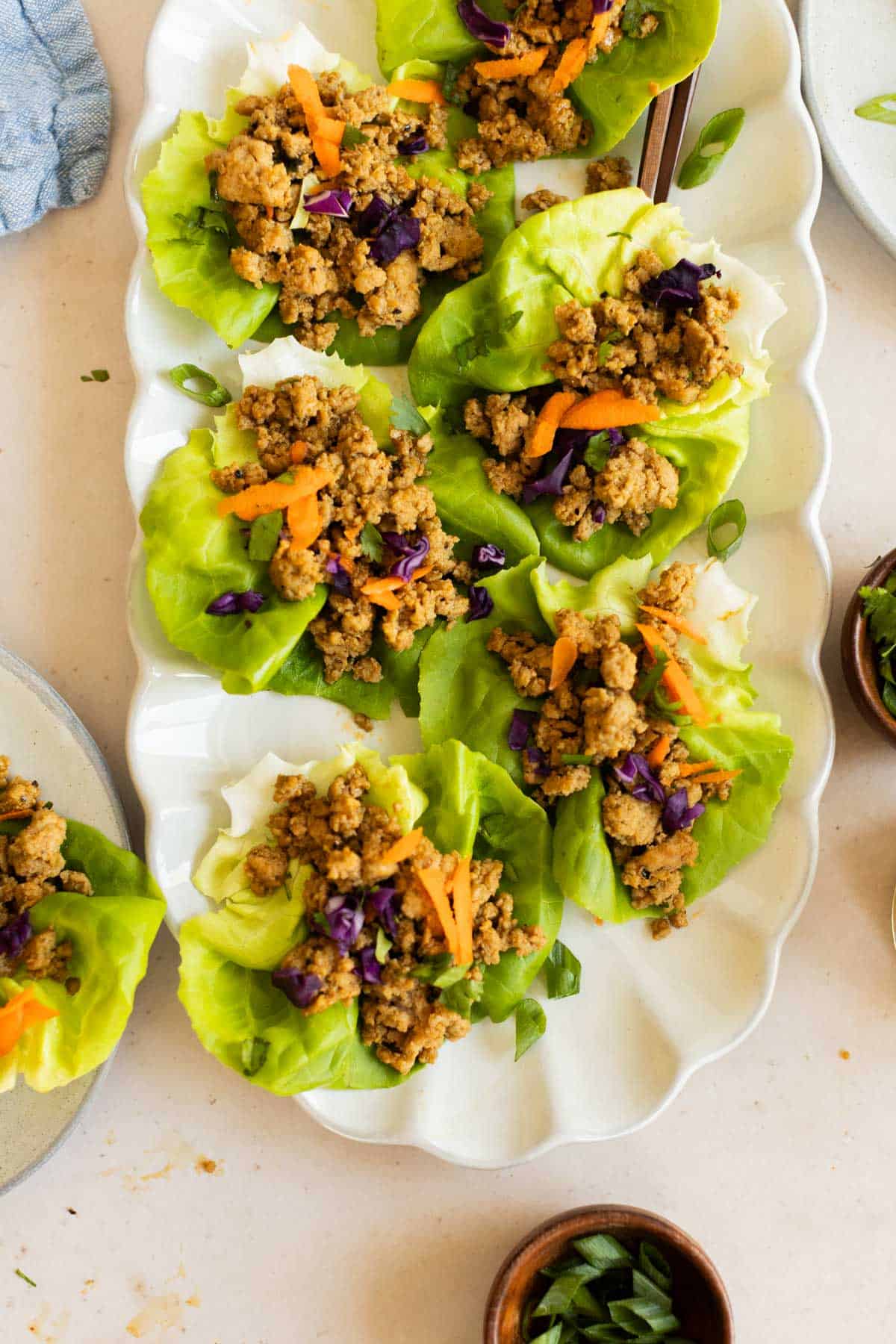 A white platter with turkey lettuce wraps filled with ground meat, shredded carrots, and purple cabbage, garnished with chopped green onions.