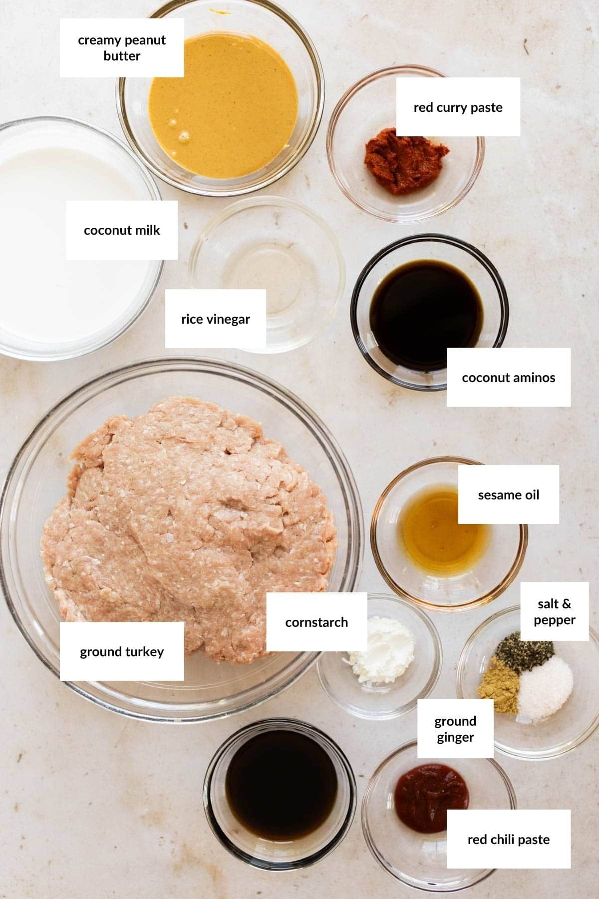 Top-down view of labeled bowls with ingredients for turkey lettuce wraps, including ground turkey, coconut milk, peanut butter, curry paste, vinegar, aminos, sesame oil, cornstarch, spices, and ginger.