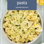 A bowl of cooked farfalle pasta with herbs, surrounded by grated cheese, with a text overlay reading "how to store pasta & reheat pasta joyfullymad.com".
