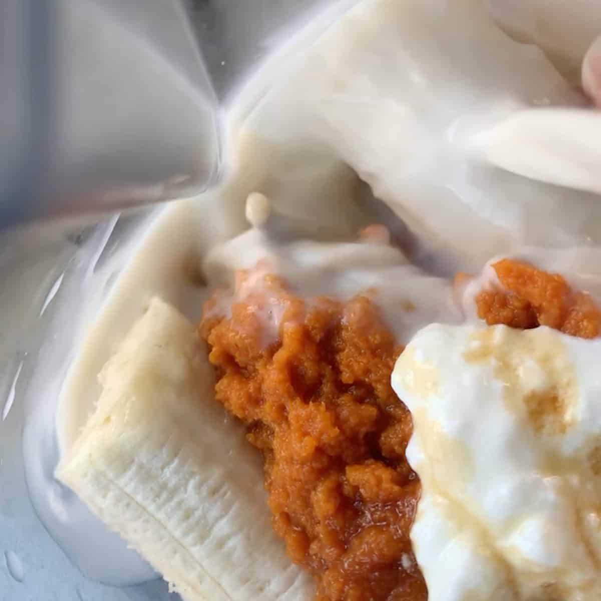 Close-up of a banana, pumpkin puree, and yogurt in a blender as milk is being poured in.