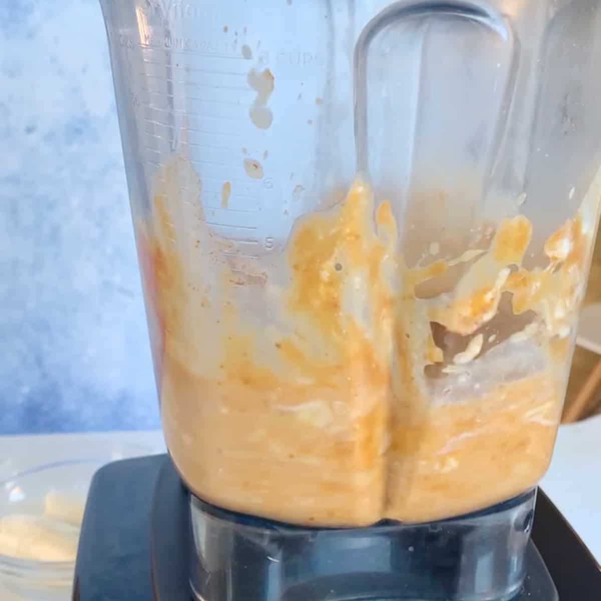 A close-up of a blender mixing an orange and creamy mixture, with some splatters on the sides of the pitcher.