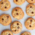 Ten chocolate chip cookies are arranged on a sheet of parchment paper, spaced apart in a grid-like pattern.