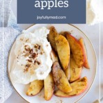 A plate with sliced cinnamon apples and a large dollop of whipped cream, garnished with chopped pecans, sits beside a striped napkin.