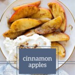 Cinnamon apples are sliced, cooked with cinnamon, and served with whipped cream on a plate, surrounded by cinnamon sticks and a checkered cloth.