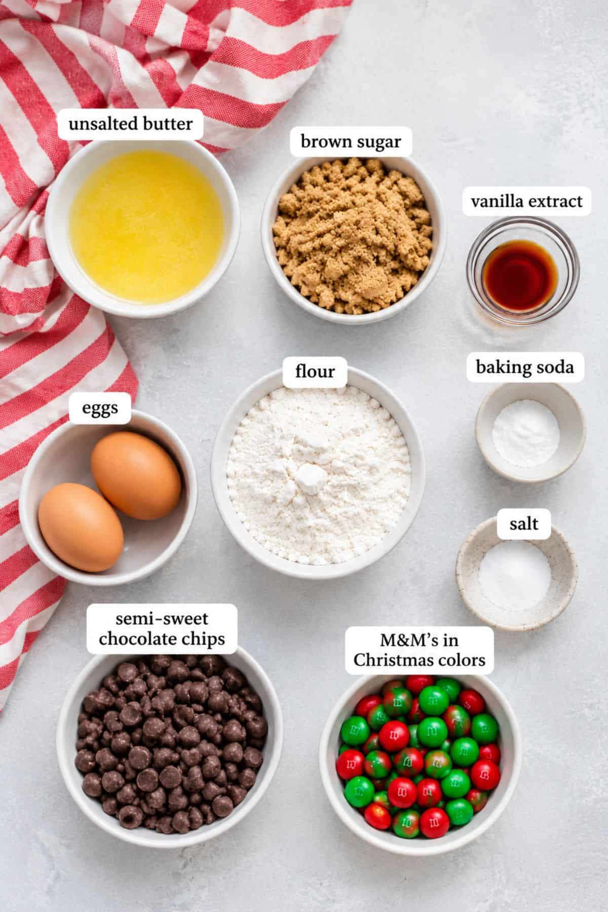 Bowls with unsalted butter, brown sugar, vanilla extract, eggs, flour, baking soda, salt, chocolate chips, and M&M’s.