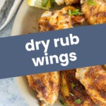 A plate of dry rub wings garnished with herbs and served with lemon wedges.