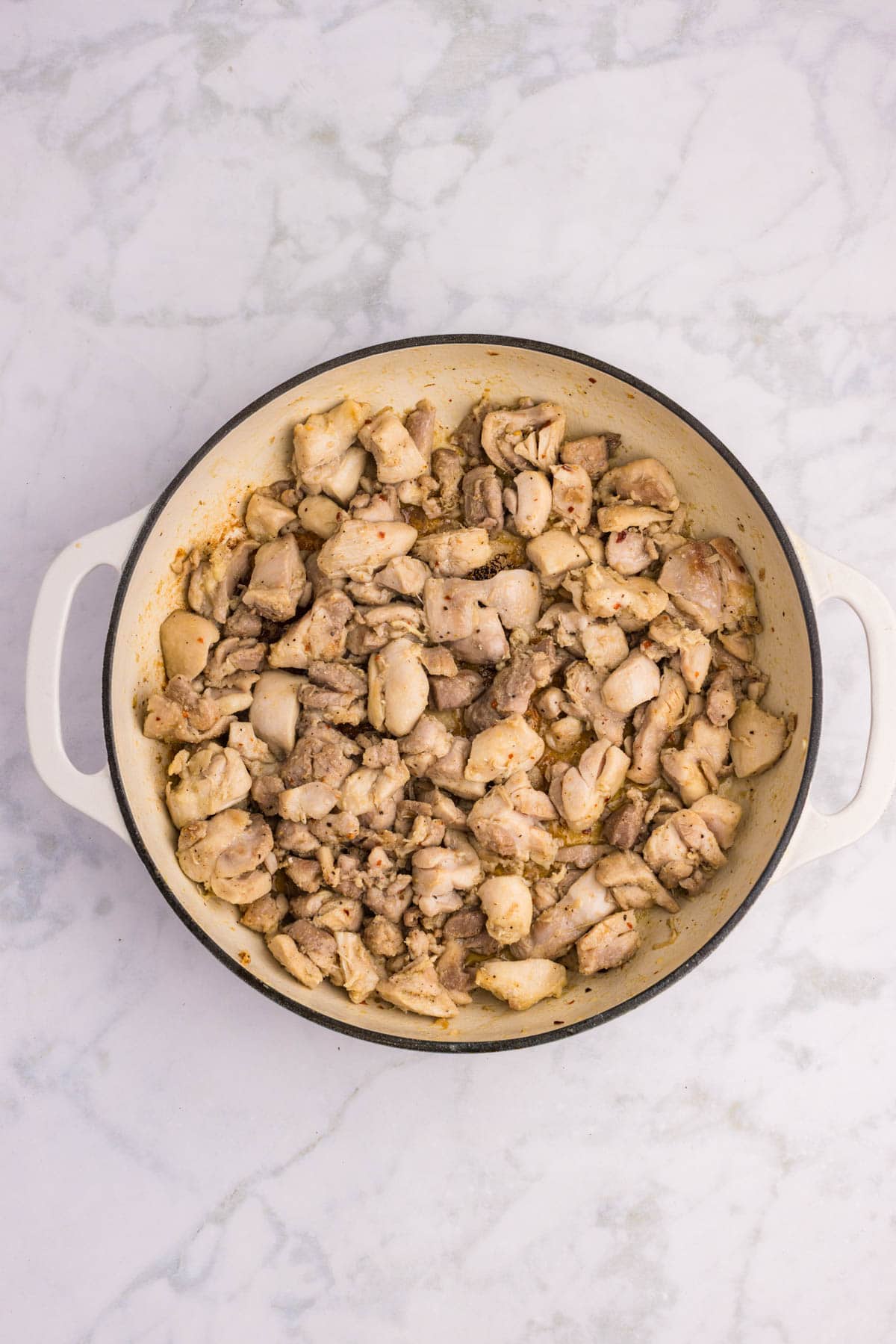 A white ceramic pot filled with cooked, diced chicken pieces sits on a white marble surface.
